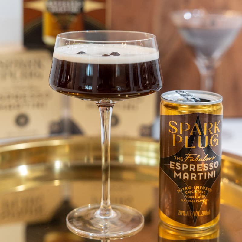A poured Spark Plug espresso martini with crema in a coupe glass beside the can on a gold tray